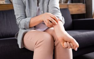 Eine Frau kratzt sich am Unterarm, vermutlich aufgrund von Hautirritationen. Ihre Unterarm ist deutlich sichtbar, während sie mit einer Mischung aus Unbehagen und Nervosität reagiert, was auf Symptome wie Juckreiz und Hautrötungen hinweist, die häufig bei Histaminintoleranz auftreten.