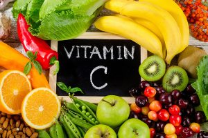 Frische vitamin-C-reiche Lebensmittel wie Kiwi, Orangen, Äpfel und Kirschen – in der Mitte eine Tafel mit der Aufschrift ‚Vitamin C‘ – symbolisiert die Bedeutung von Vitamin C als Antioxidans und Immununterstützer gemäß dem Ratgeber von VitaPart®.