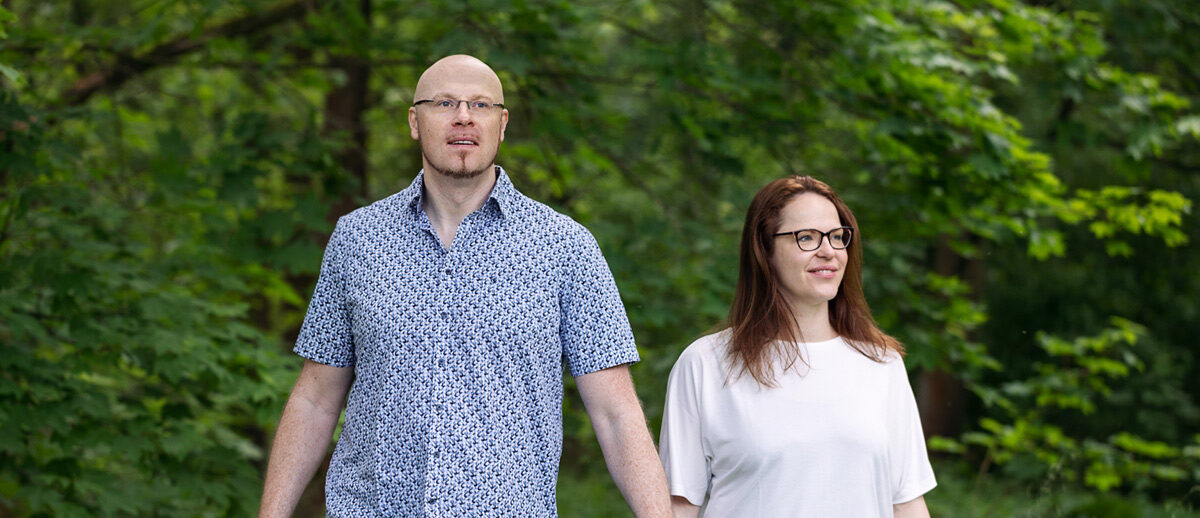 Dr. Steffen Jakobs und Anne Kayser stehen lächelnd nebeneinander vor grünem Waldhintergrund. Beide blicken nicht direkt in die Kamera, sondern lassen ihre Blicke ruhig in die Ferne schweifen. Ihre entspannte und natürliche Haltung unterstreicht ihre enge Verbindung zur Natur, die auch ihre Arbeit bei VitaPart® prägt – einer Marke, die traditionelle Pflanzenkunde mit moderner Wissenschaft verbindet.