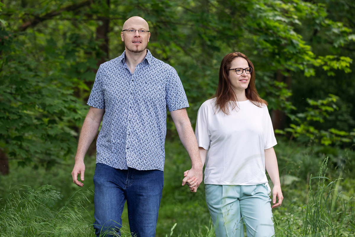 Dr. Steffen Jakobs und Anne Kayser stehen lächelnd nebeneinander vor grünem Waldhintergrund. Beide blicken nicht direkt in die Kamera, sondern lassen ihre Blicke ruhig in die Ferne schweifen. Ihre entspannte und natürliche Haltung unterstreicht ihre enge Verbindung zur Natur, die auch ihre Arbeit bei VitaPart® prägt – einer Marke, die traditionelle Pflanzenkunde mit moderner Wissenschaft verbindet.